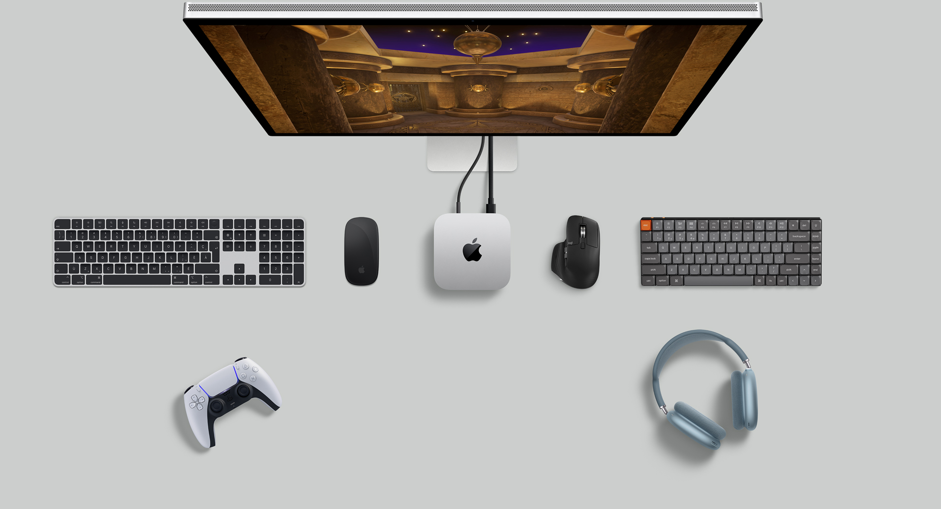 Vue du dessus d’un Mac mini argent sur un bureau avec un écran, des claviers sans fil, une souris sans fil, une manette de jeu et des AirPods Max