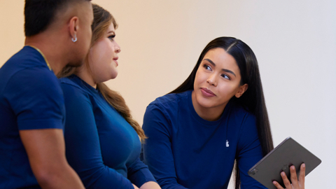 Three Apple Retail employees talking together, one holding an iPad.