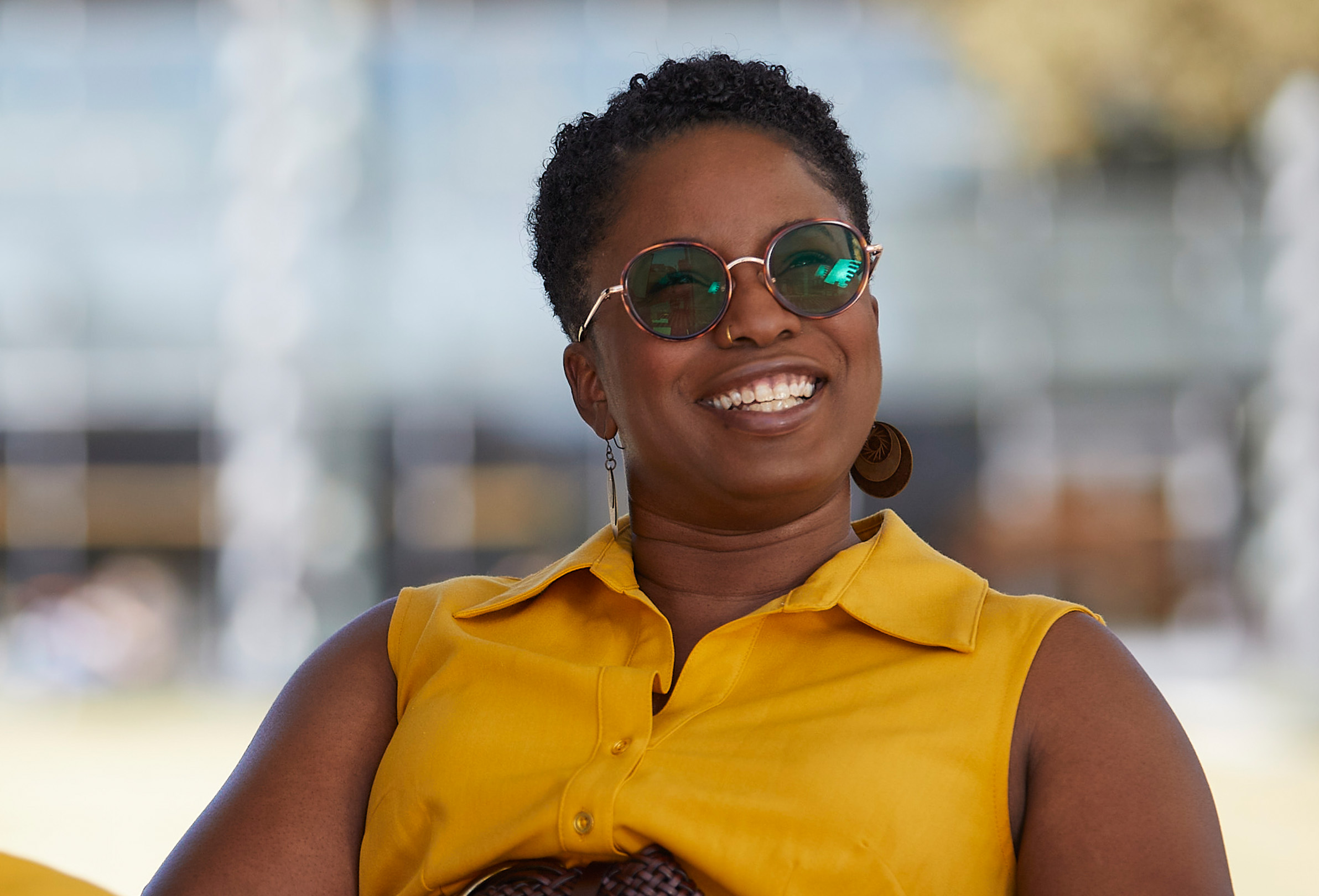 Une employée d’Apple assise dehors avec des lunettes de soleil sourit.