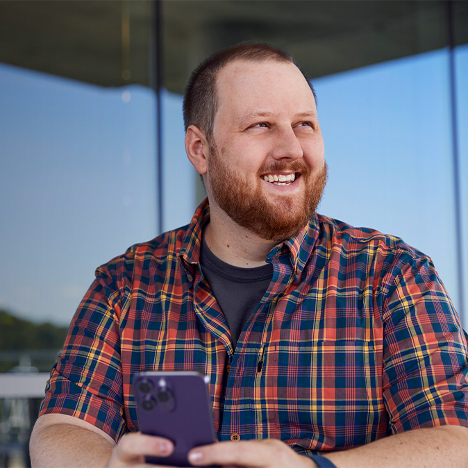 Topher, assis devant un immeuble de bureaux, regarde vers le côté en souriant.