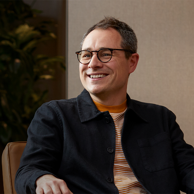 Dan smiling, sitting in an armchair and looking at someone to his right.