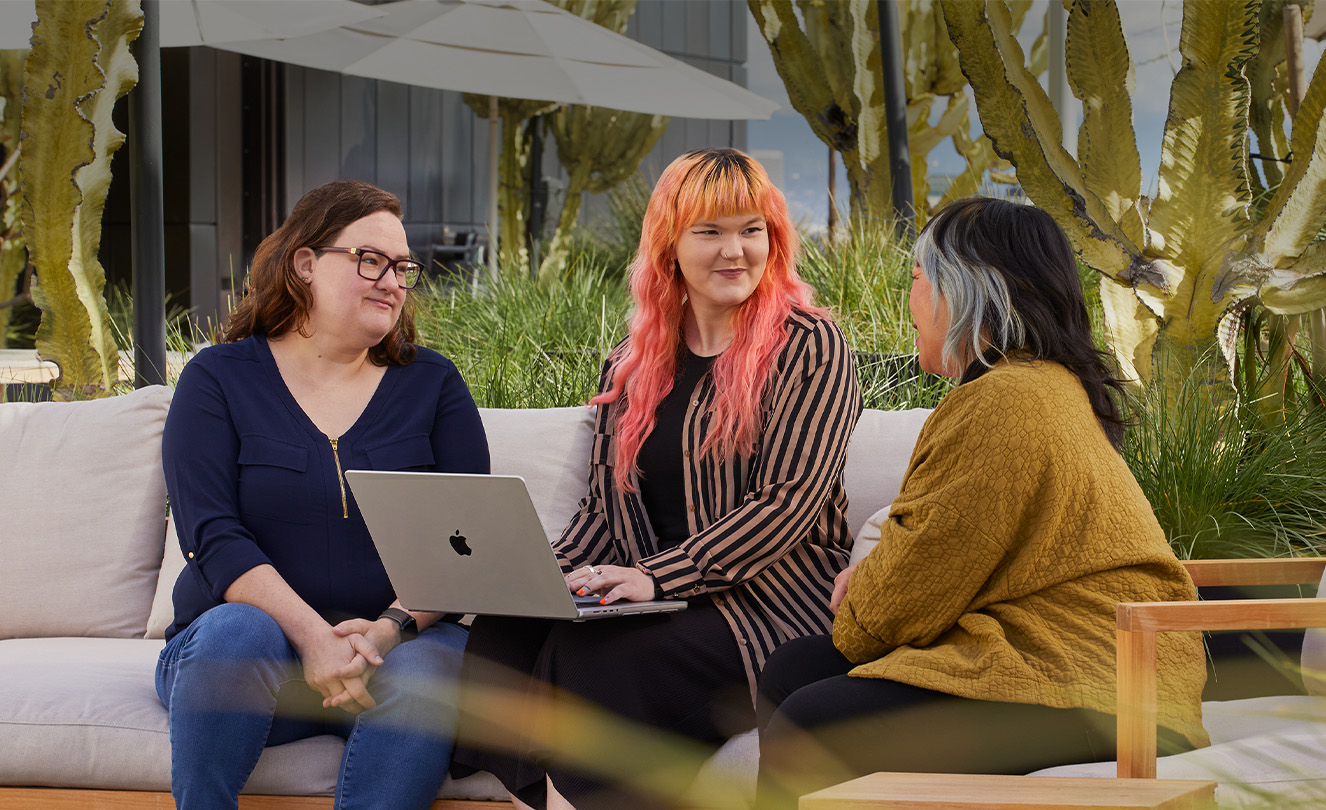 Trois employées d’Apple assises ensemble sur une terrasse, l’une d’elles avec un MacBook.