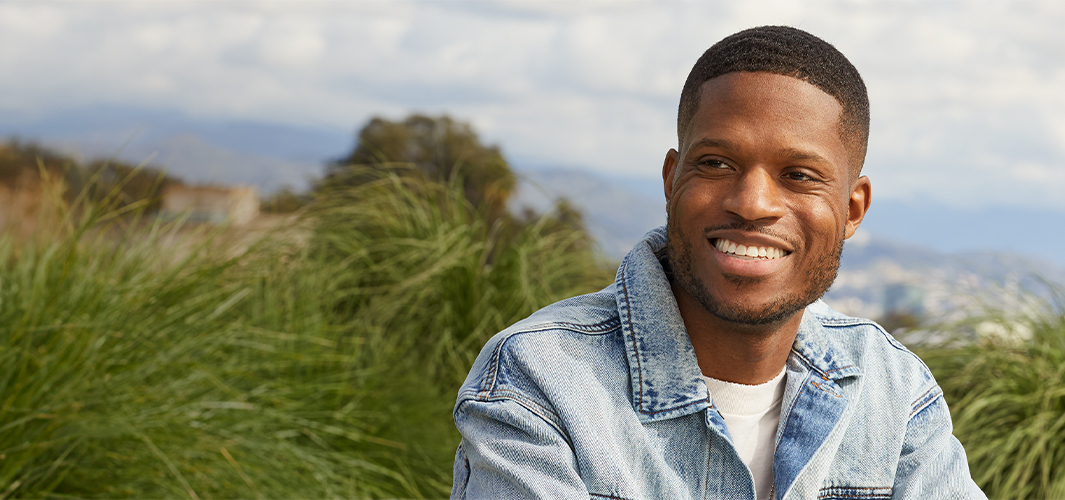 Justin souriant, assis sur une terrasse, avec le ciel et des arbres en arrière-plan.