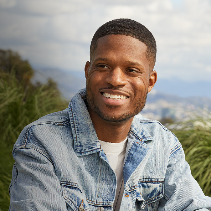 Justin souriant, assis sur une terrasse, avec le ciel et des arbres en arrière-plan.