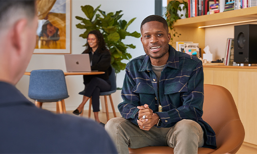 Justin assis à l’intérieur dans un  bureau, en train de parler avec un collègue d’Apple.