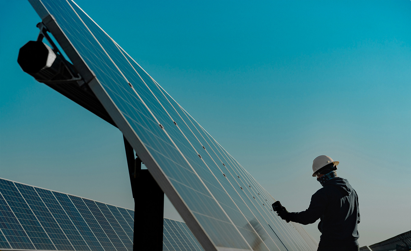 Un homme portant un casque de protection travaille sur un grand panneau solaire en extérieur.