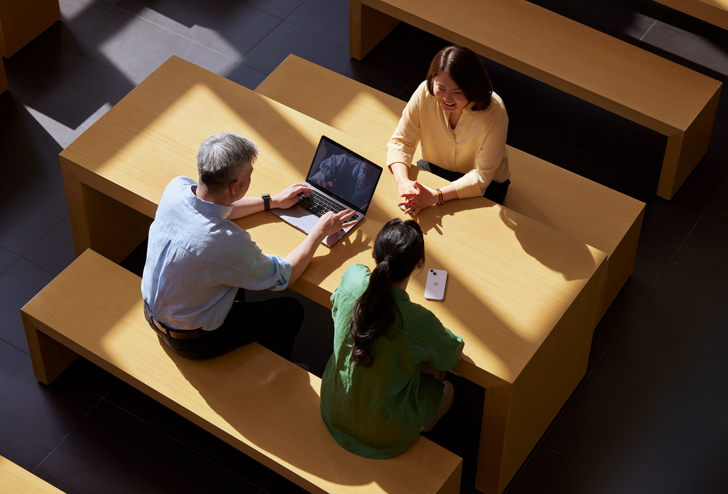 Three Apple employees sitting together while one works on a MacBook.