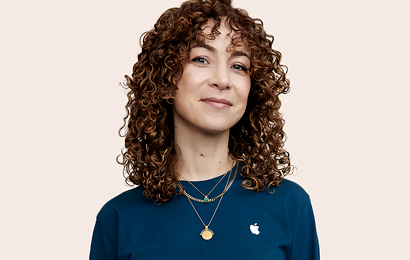 Membre de l’équipe Apple Retail avec des cheveux frisés, qui regarde l’objectif.