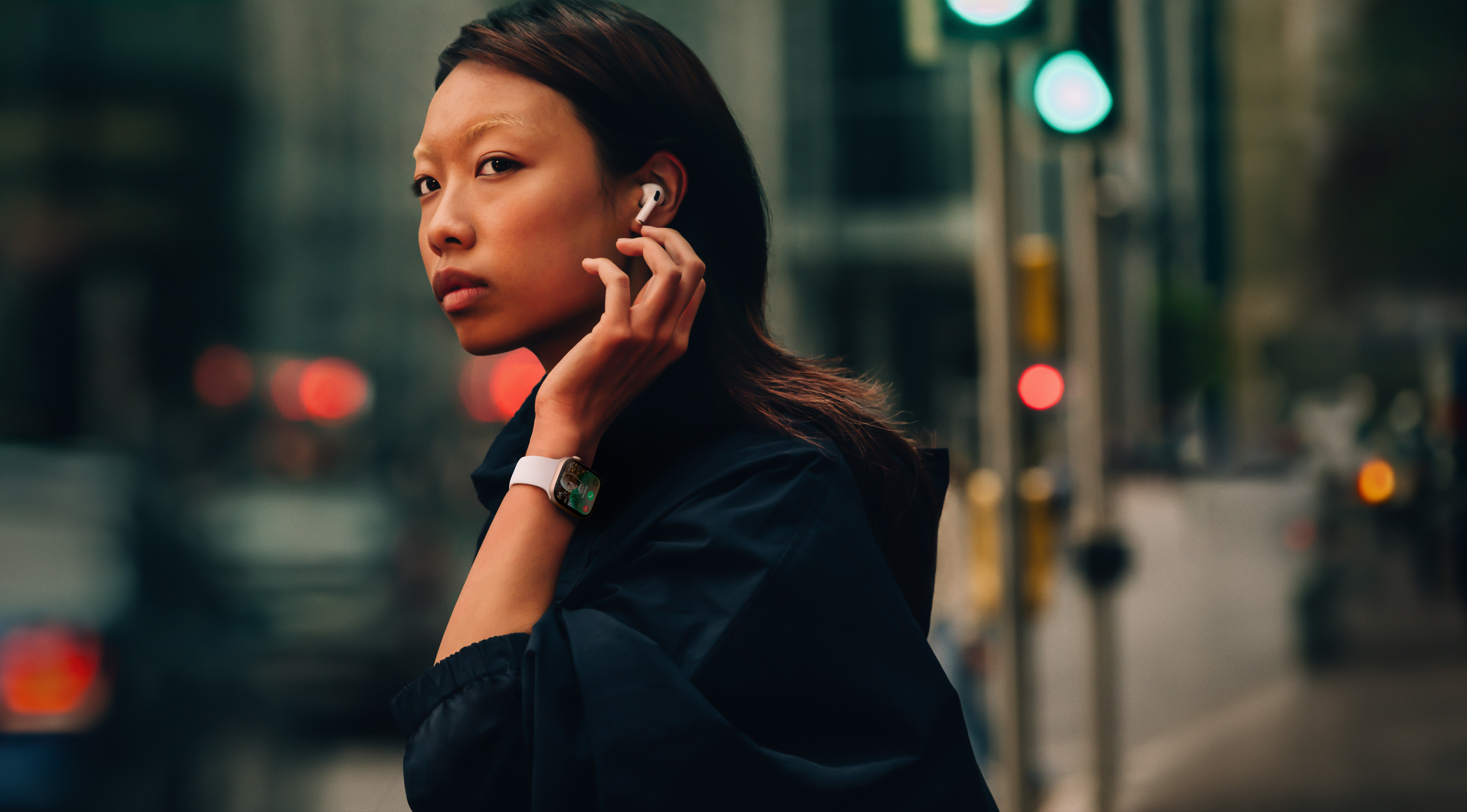 A woman on a street wearing Apple Watch Series 10 and AirPods.