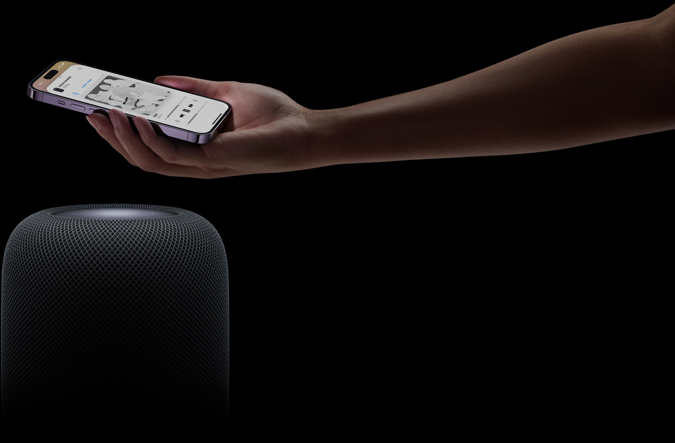 A hand coming in from the right side of the page holds an iPhone above a HomePod speaker