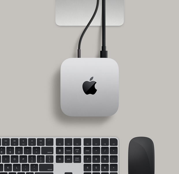 銀色 Mac mini 俯視圖，兩條連接線從背面插口連接至一部顯示器，旁邊放有黑色精妙滑鼠和黑色精妙鍵盤。