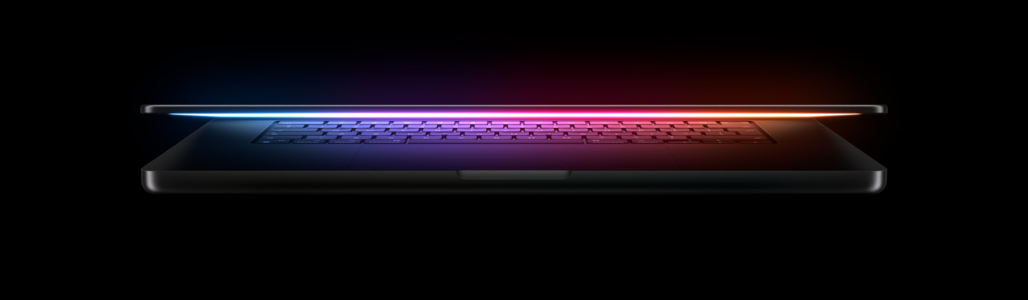 A slightly open MacBook Pro casts a multicolored glow from the screen onto the keyboard