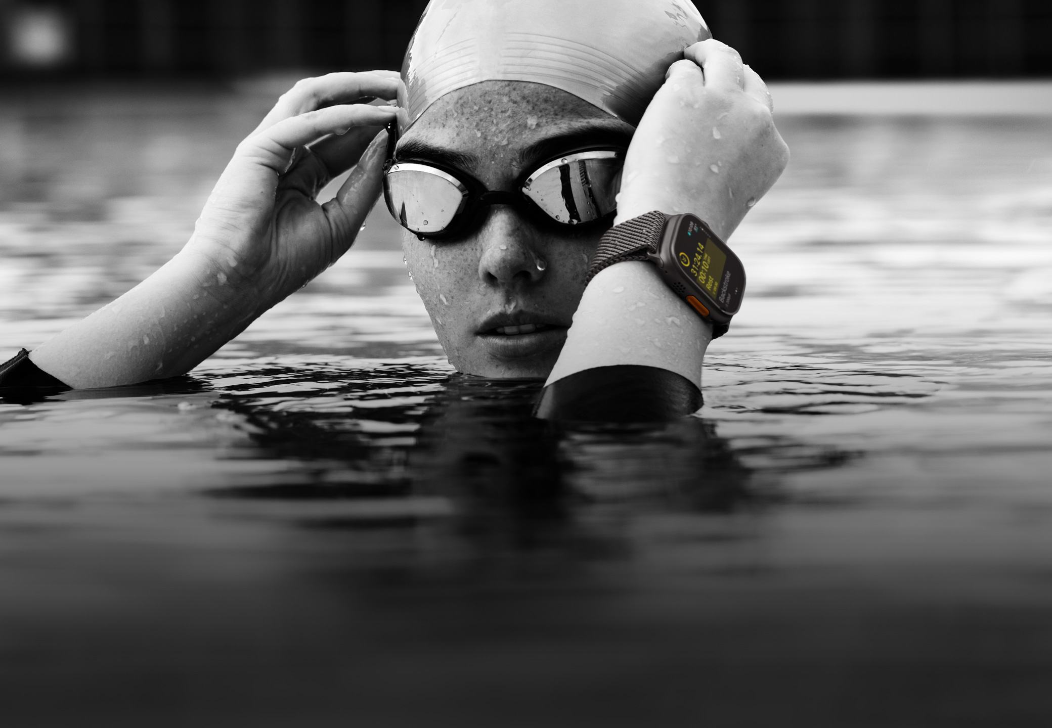 Kopf und Hände einer Schwimmerin über dem Wasser in einem Pool, die eine Apple Watch Ultra 2 trägt und ihre Schwimmbrille zurechtrückt.